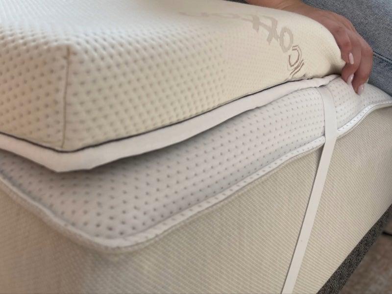 A woman sits on the edge of the Saatva Graphite Memory Foam mattress topper