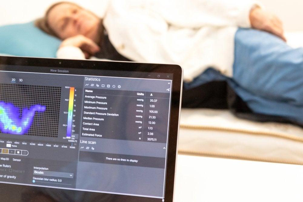 A woman lays on her side on a pressure map while someone captures data on a computer