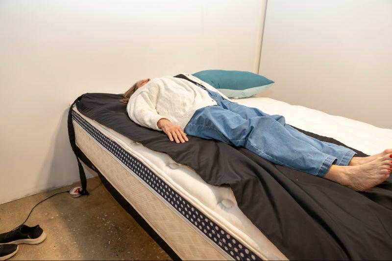 A woman lying on a pressure relief mat placed over the WinkBed Luxury Firm mattress