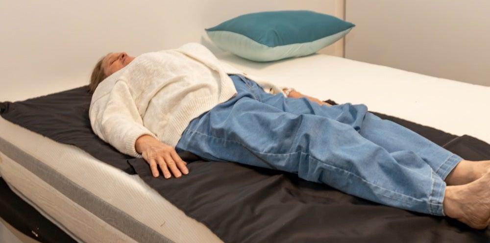 Woman lies on her back on a black pad on top of a white mattress