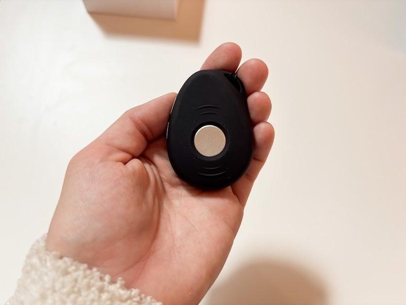 The LifeStation Sidekick is a black oval roughly the size of a large chicken nugget. It looks like a car key fob. There is a dime-sized silver button in its center.