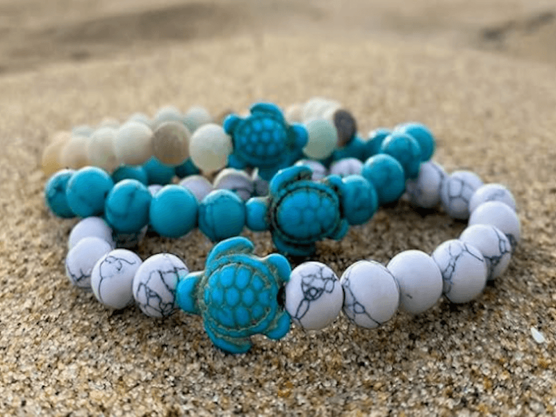 Three beaded bracelets with turtle charms displayed on sand