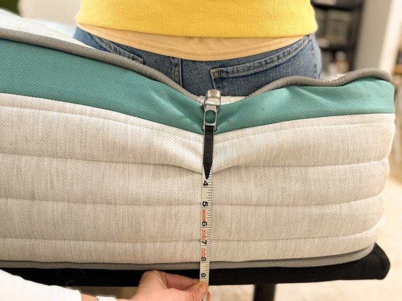 A measuring tape shows the compression of the Helix Sunset mattress when a tester sits on the edge.