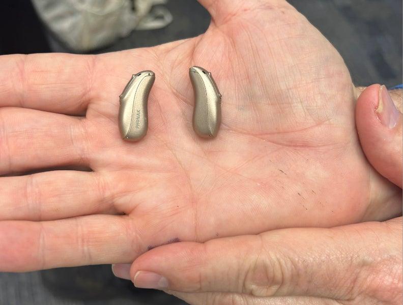 A hand holding two Phonak Lumity hearing aids