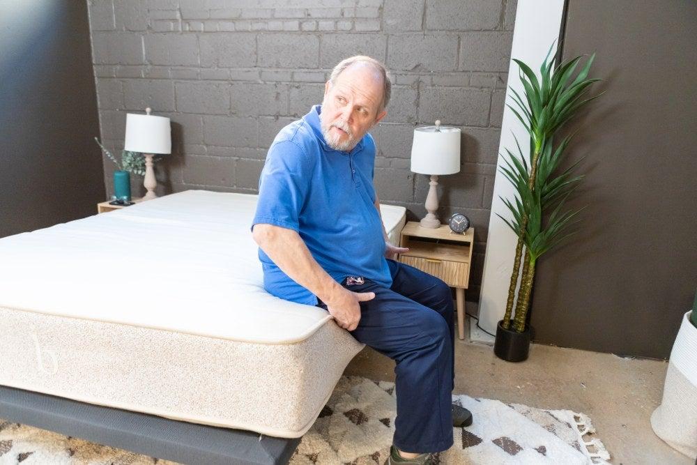 An older adult man sitting on the edge of the Birch Natural mattress