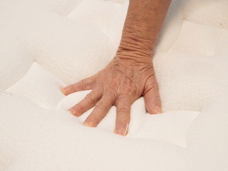 A hand pushes down on the plush top of the Nolah Evolution Luxury Firm mattress.