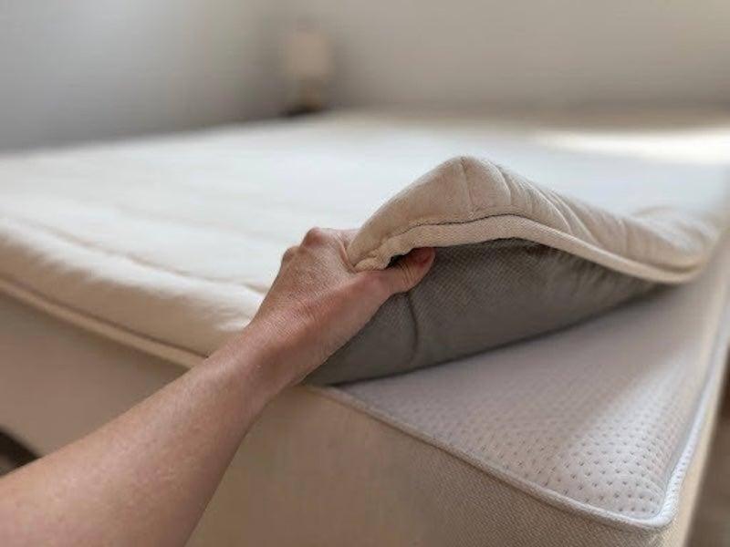 Someone lifting the corner of the Birch Plush Organic mattress topper