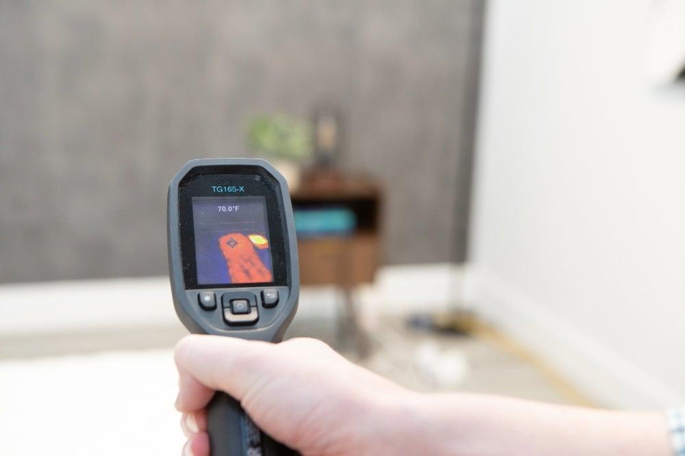 Man holds temperature gun in his right hand to measure the surface temperature of the Titan Plus mattress