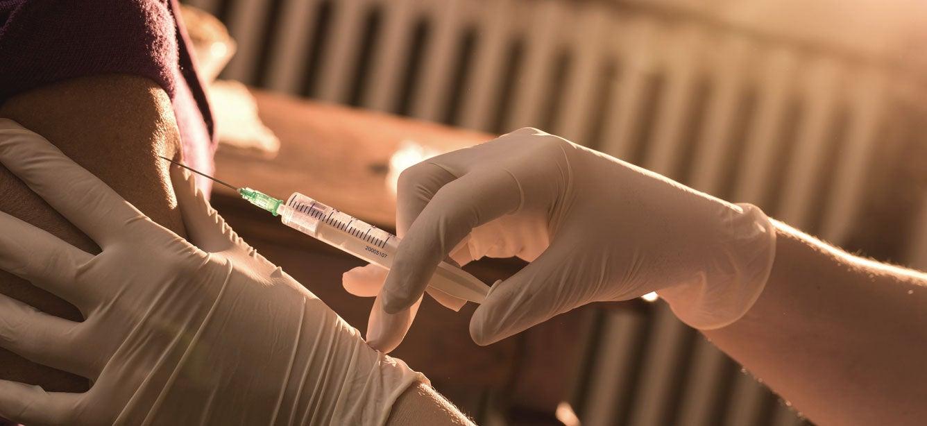 An up close shot of a nurse is giving a senior Black woman a flu shot.