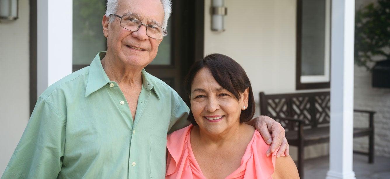 Smiling older couple standing together outside a house, with the man�s arm around the woman�s shoulder.