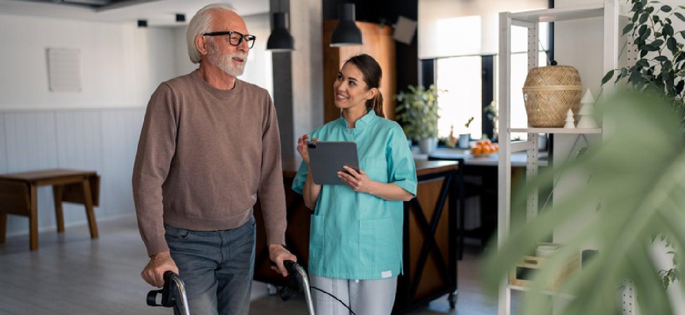 An older man with black glasses is walking with assistance and talking to a worker who is smiling. He has made good choices for long-term care by purchasing long-term care insurance. Long-term care insurance costs vary based on factors like age, health, and coverage. Find out the average cost of a policy today and what to consider when shopping around.