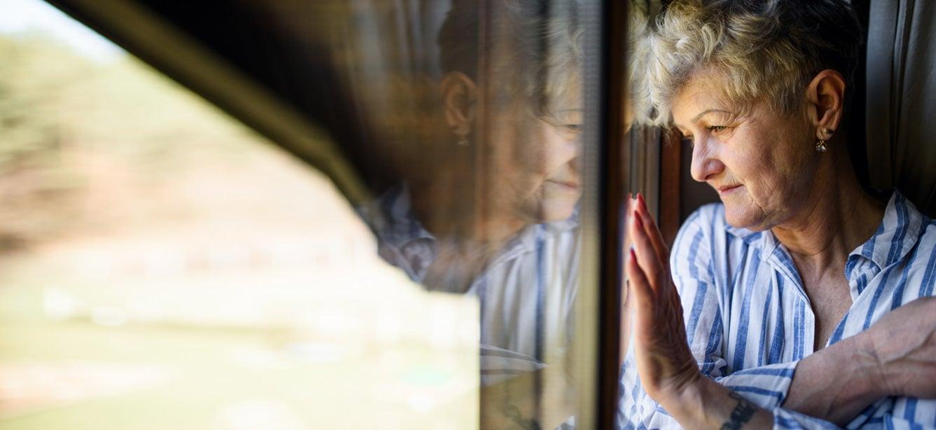 A senior Caucasian woman is at home during the pandemic, staring outside of her window.