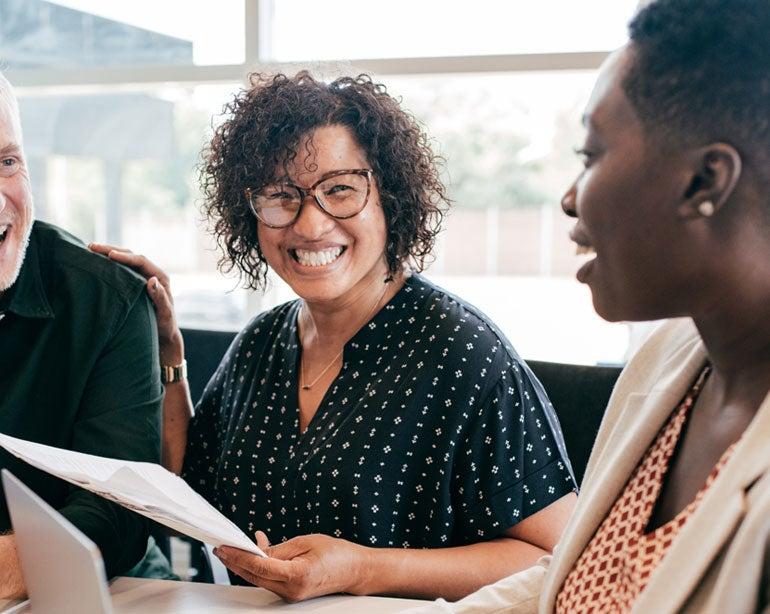 A diverse group of professionals are having a meeting, sharing stories and laughing.