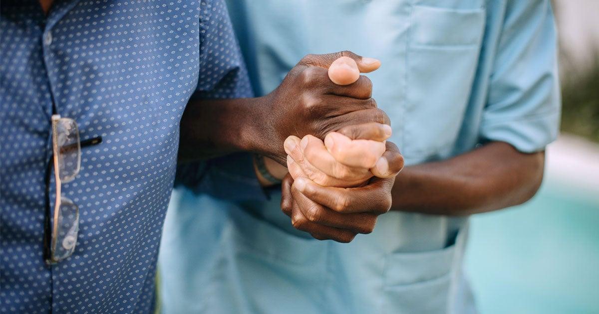A male nurse is helping a Black senior man walk in a nursing home.