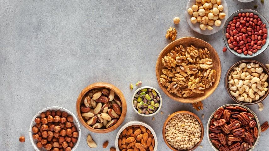 overhead view of eight bowls of nuts including almonds, cashews, and pistachio