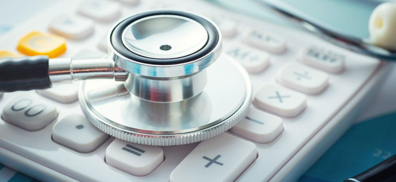 A close up shot of a stethoscope laying on top of a calculator, indicating the cost of health care.
