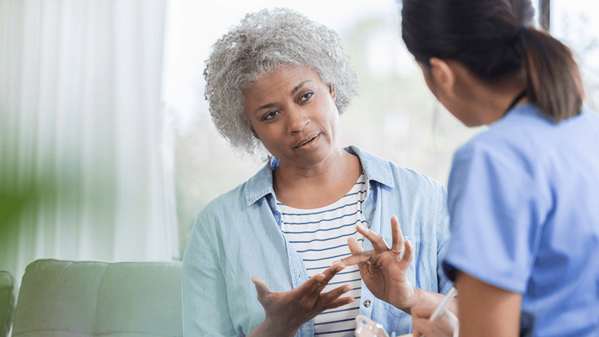 black woman with gray curly hair talking with dark haired woman in medical scrubs
