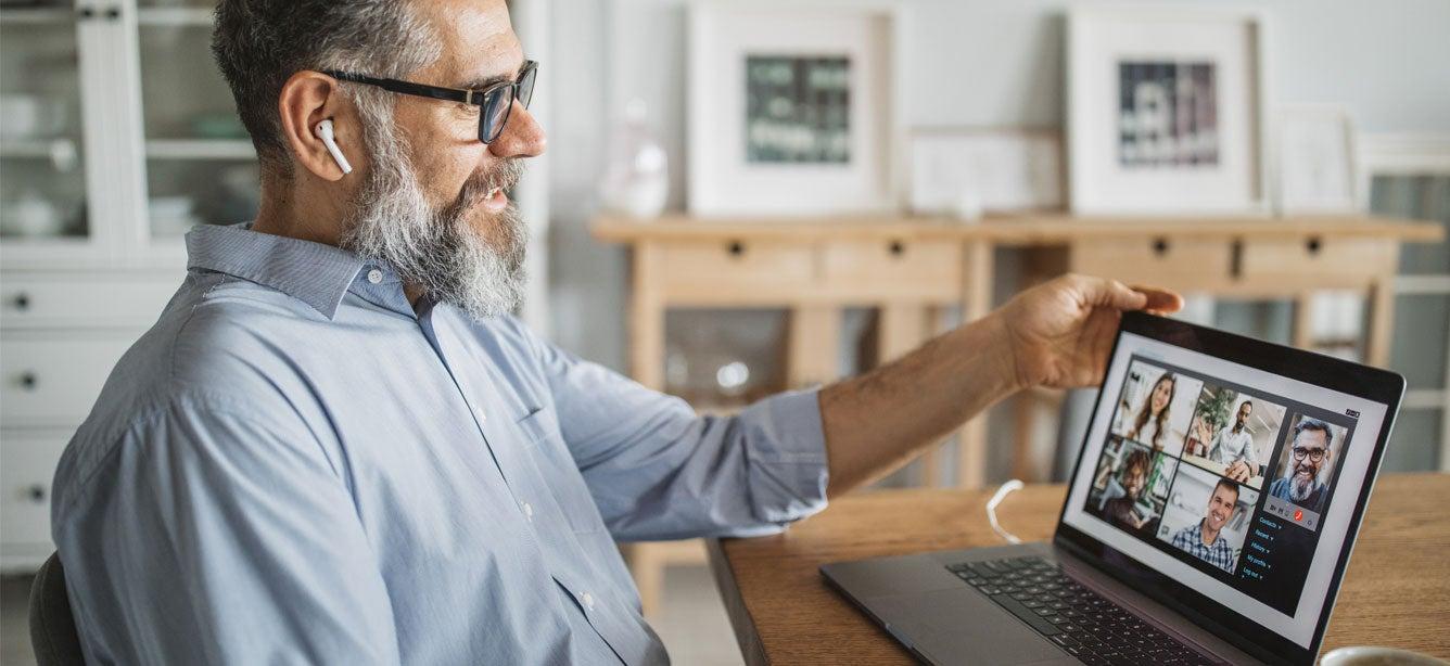 A man with a beard and glasse smiles while using a laptop for a video call.