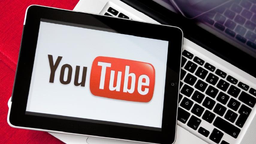 Tablet sitting on top of a laptop. On the tablet's screen is the YouTube homepage.