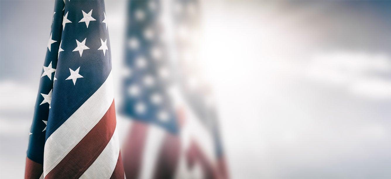 American flags gently waving, featuring red and white stripes and white stars on a blue field, against a blurred background
