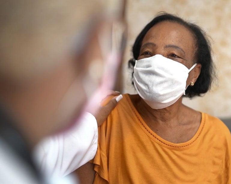 A Black senior woman wearing a mask is looking on at her doctor that's giving her advice.