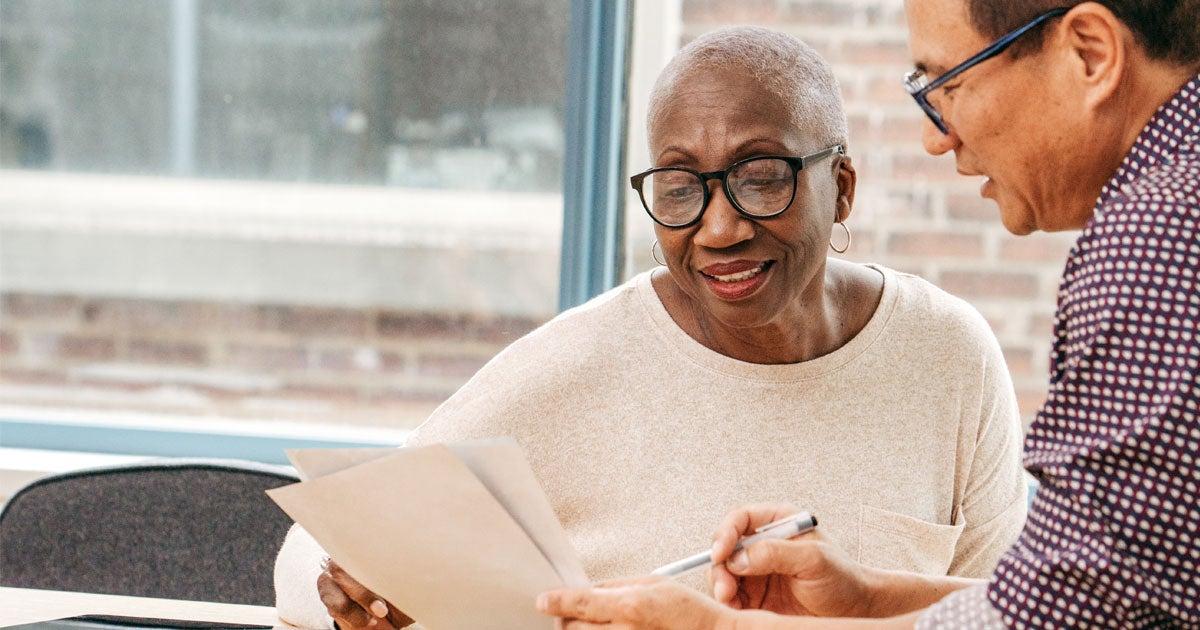 An older Black female professional is discussing Medicare benefits with an Asian male colleague.