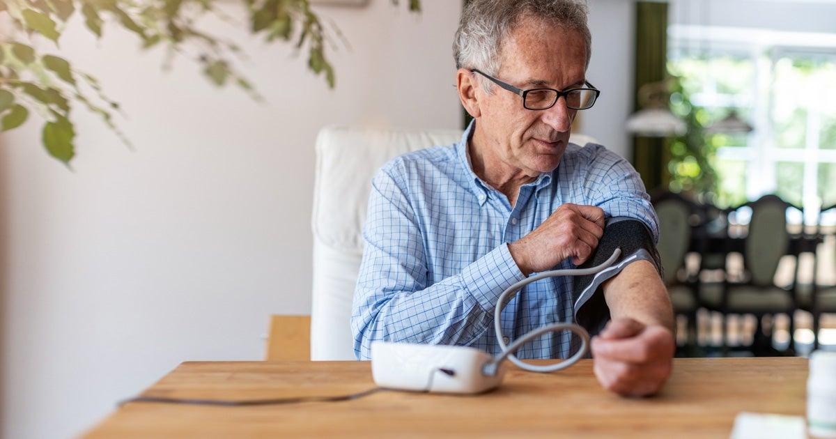 A senior man is sitting down at the kitchen table using a medical device to measure his blood pressure.