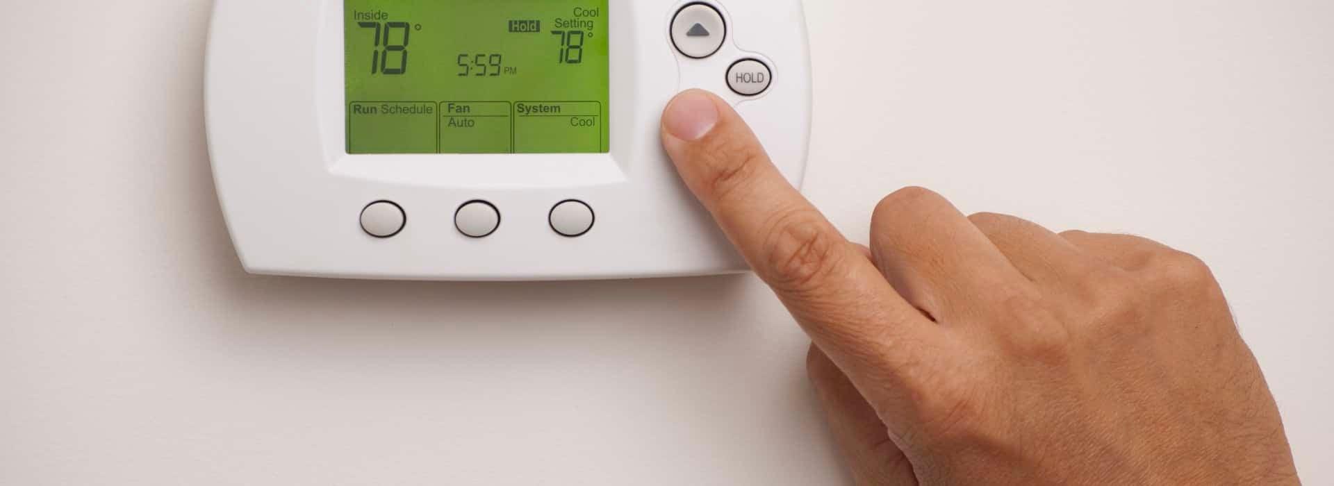 Person's finger setting home energy temperature using a digital thermostat