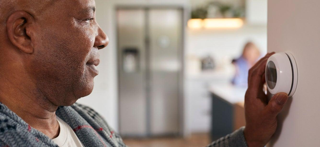 A senior Black man is adjusting the thermostat at home.
