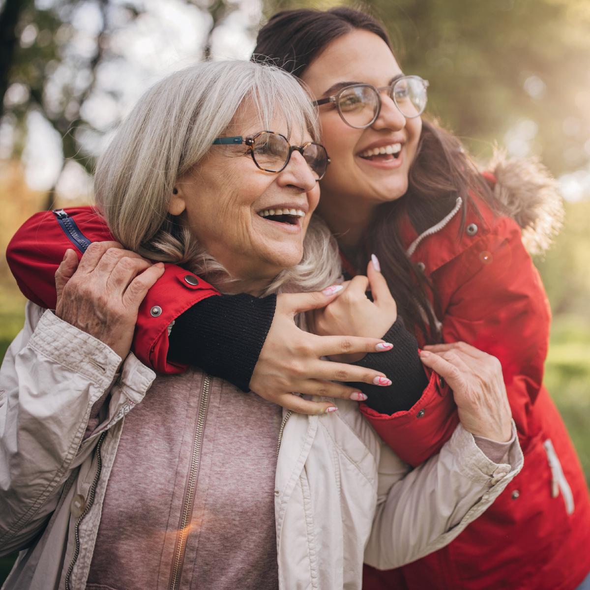 A younger woman is hugging her grandmother, both are smiling.
