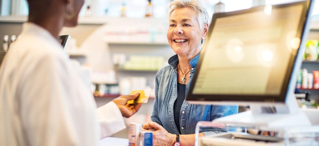 A smiling older woman gives her card to a pharmacist at the checkout counter