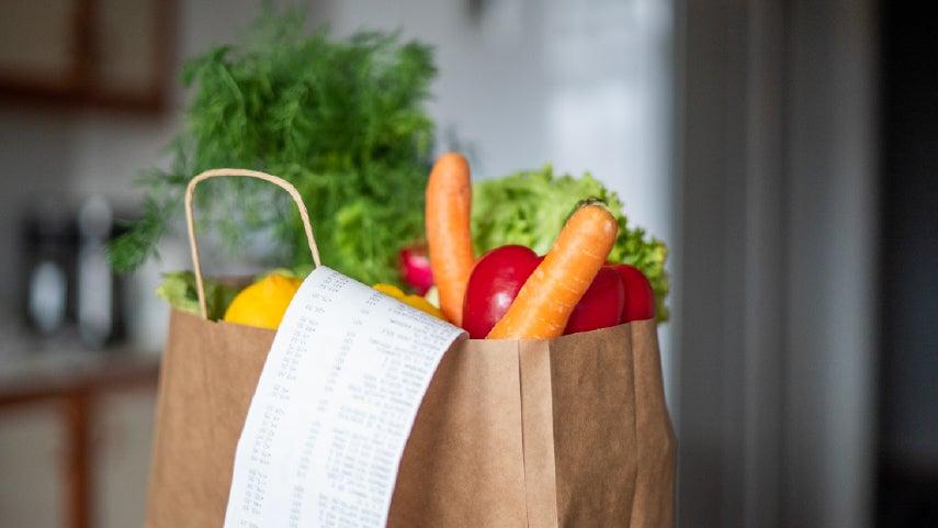 A brown paper bag holding colorful groceries, with a long receipt hanging out of the bag.