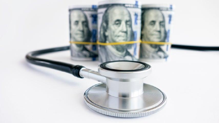 Money wrapped in bands, sitting in front of a stethoscope.