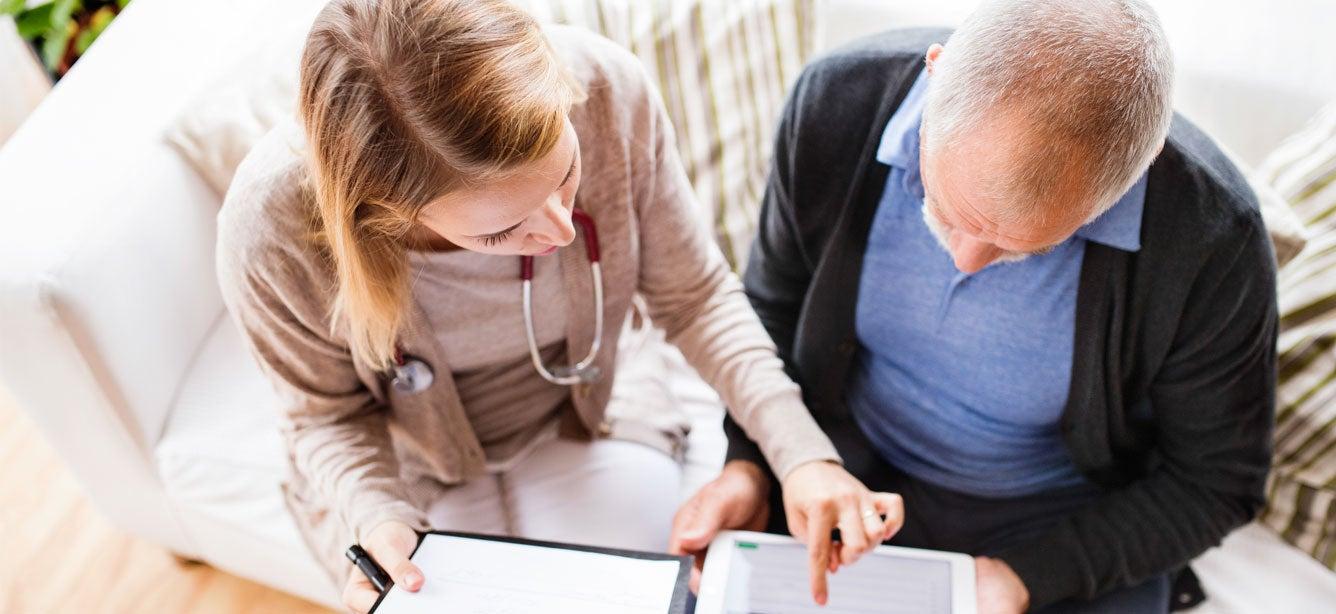 A health advisor and a senior man with a tablet have a conversation about his health care with a tablet.