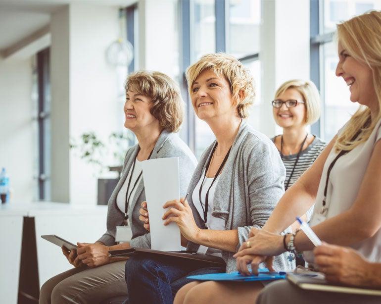 An older senior center professional is engaged and listening to a speaker with her peers during a seminar.
