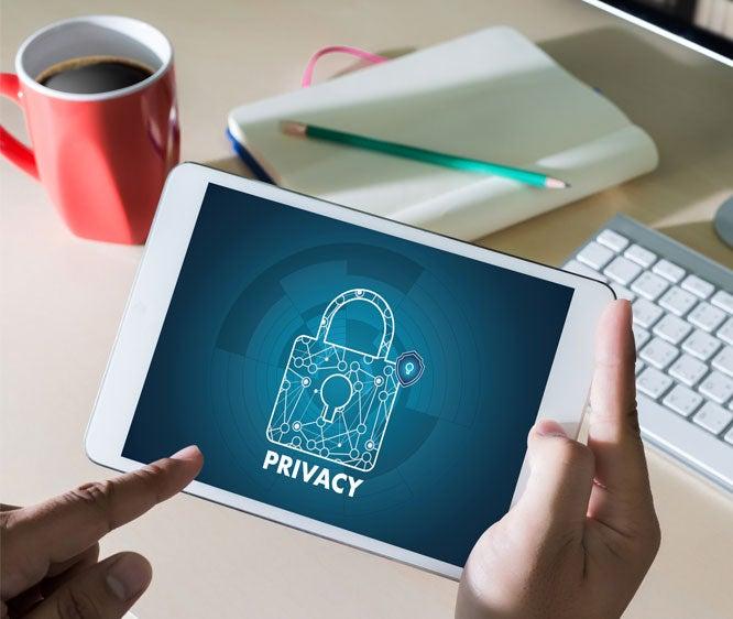 A close up of hands holding a tablet that has an image of a lock and the word "privacy" underneath it.