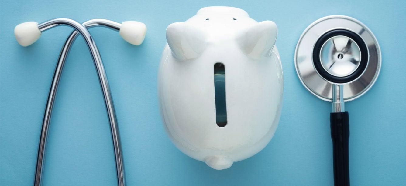 A close up shot of the parts of a stethoscope surrounding a white, porcelain piggy bank on a light blue background.