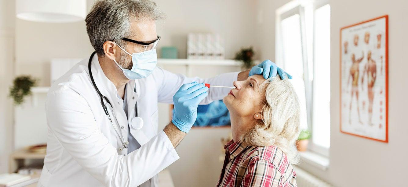 A doctor takes a nasal swab from a senior woman for genetic testing.