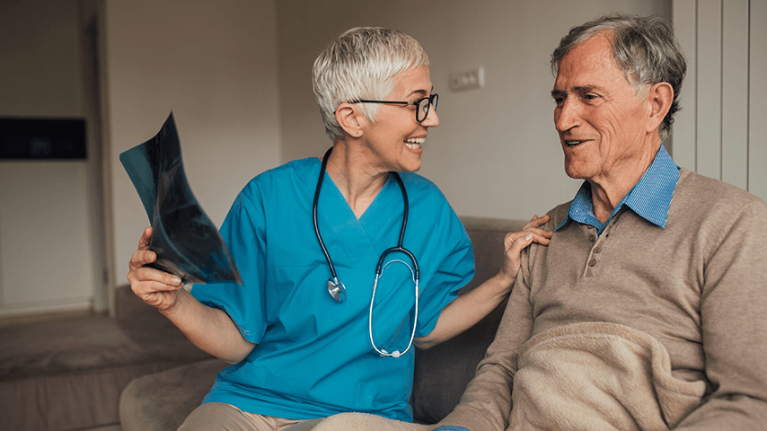 smiling medical provider wearing stethoscope and holding x-ray with hand on shoulder of smiling older man