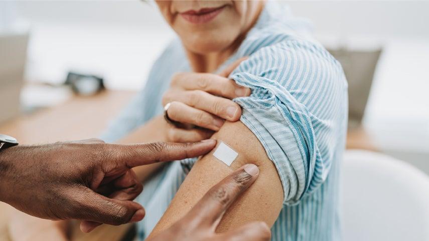 A older caucasian woman just got her shingles vaccine and is putting a bandaid on.